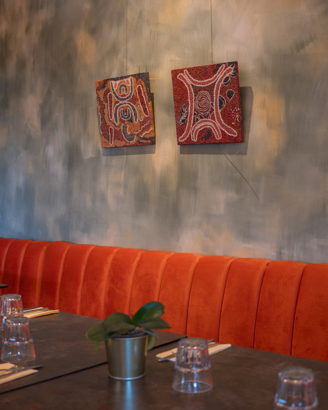 Intérieur bistrot chic, banquette orange, table dressée, plantes et tableaux abstraits, ambiance authentique.