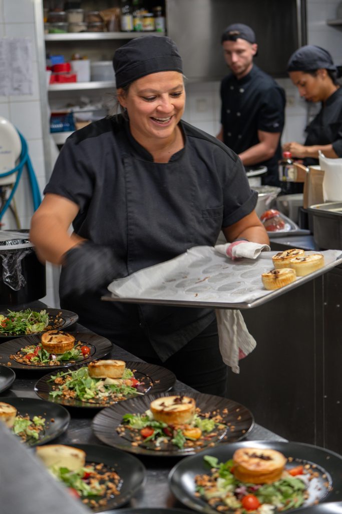 Chef en noir dresse des tartes sur salade au Restaurant Le Progrès, lieu emblématique de Bormes-les-Mimosas.