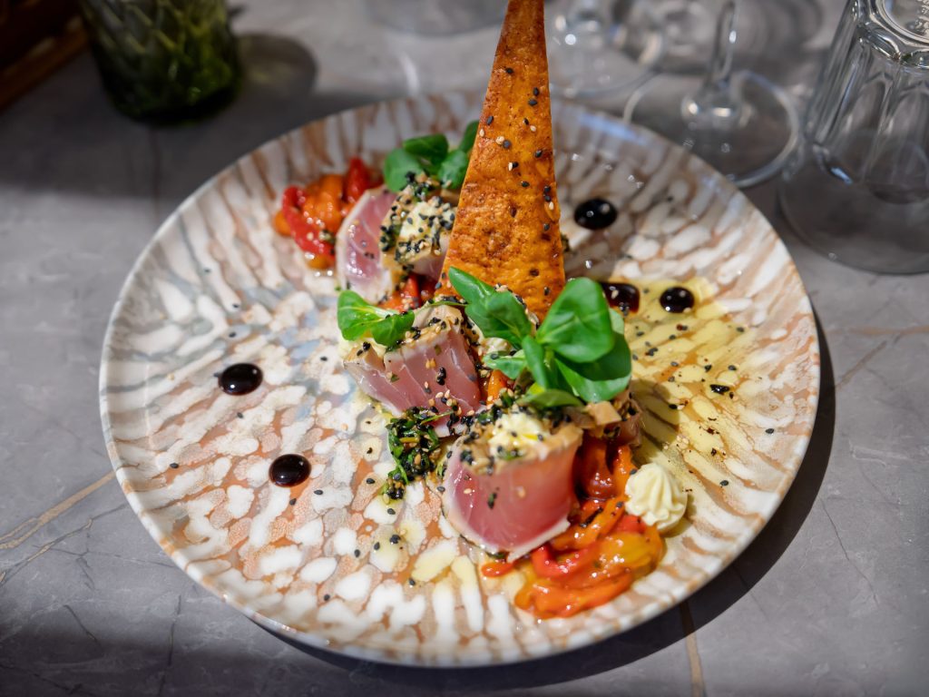 Thon mi-cuit au sésame, légumes grillés, croquant maison, le tout présenté sur une assiette en faïence.