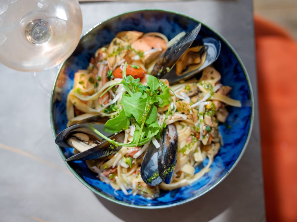 Pâtes aux fruits de mer, moules, crevettes et légumes verts, servies dans une assiette bleue ancienne.