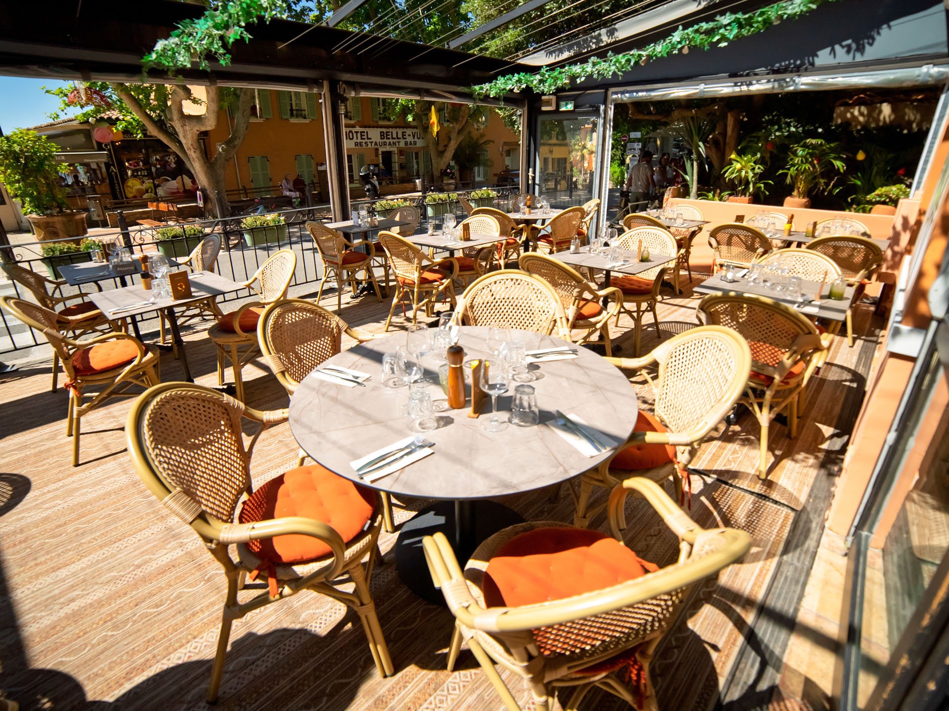 Terrasse historique du Progrès, tables dressées sous la pergola, chaises en osier orange, lumière du Midi.