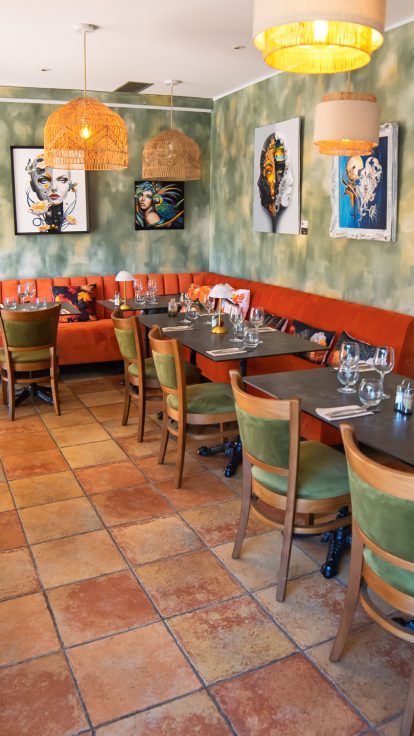 Une salle chaleureuse, des banquettes orange, des chaises vertes, une décoration éclectique et un charme historique indéniable.