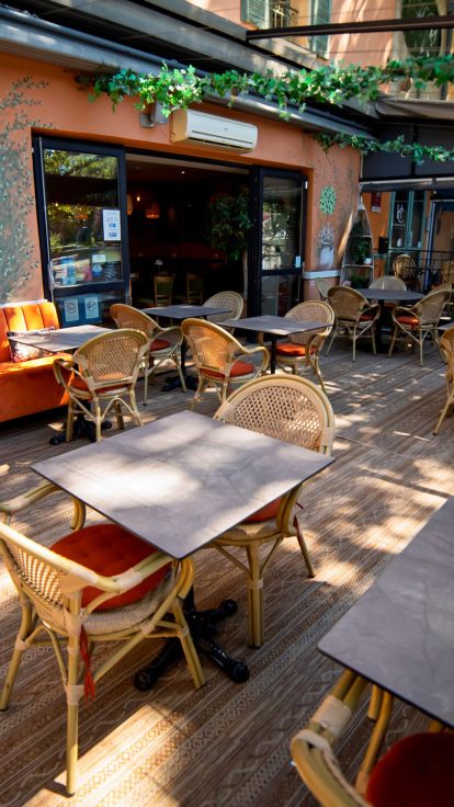 Terrasse historique du Café du Progrès, chaises en osier vides sous le auvent, ambiance traditionnelle préservée.